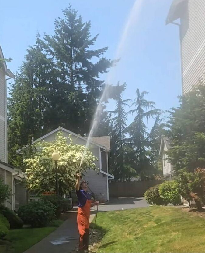 Deep Water technician soft washing the upper siding of an apartment community from the walkway