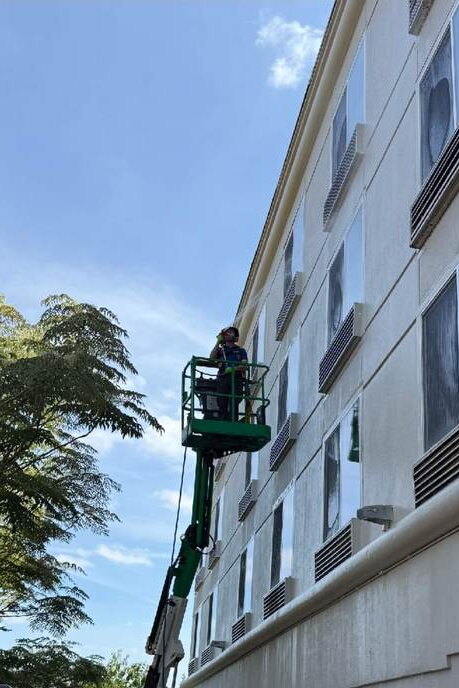 Deep Water technician soft washing the upper walls of a Queen Anne building from a lift