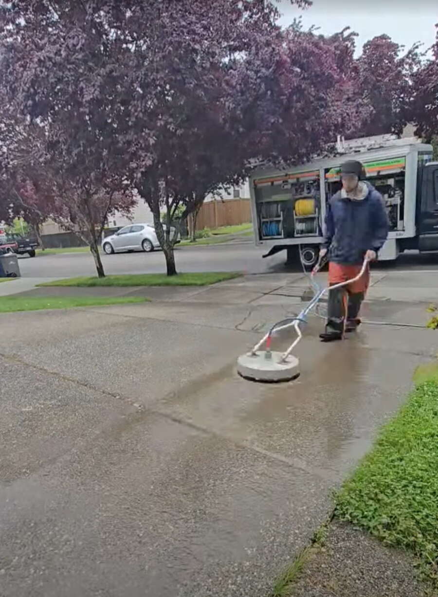 Deep Water technician surface cleaning a residential driveway with the service rig parked behind