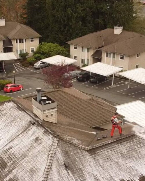 Deep Water technician soft washing the roof of a condominium building above the community carports