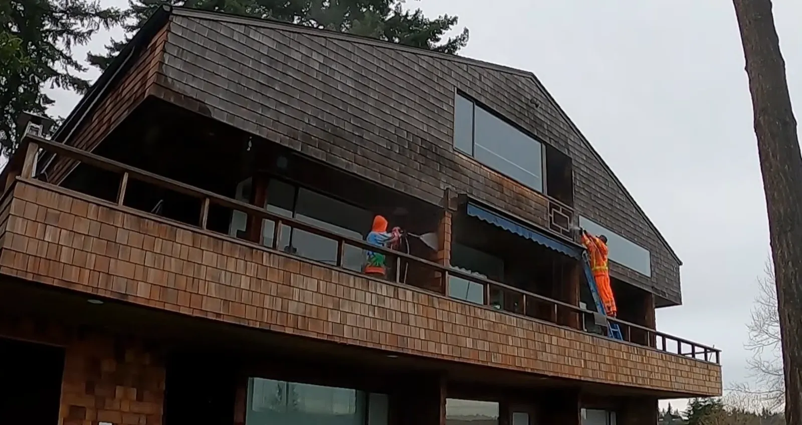 Two Deep Water technicians soft washing the cedar siding of a two-story home