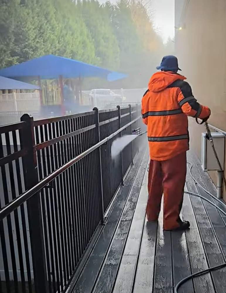 Deep Water technician pressure washing a patio walkway and iron railing in Bellevue