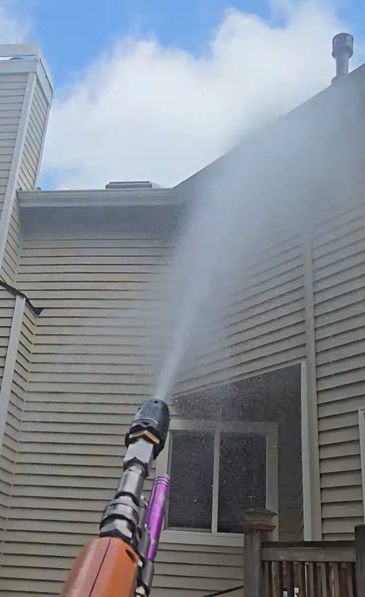 Soft wash spray rinsing algae from painted lap siding