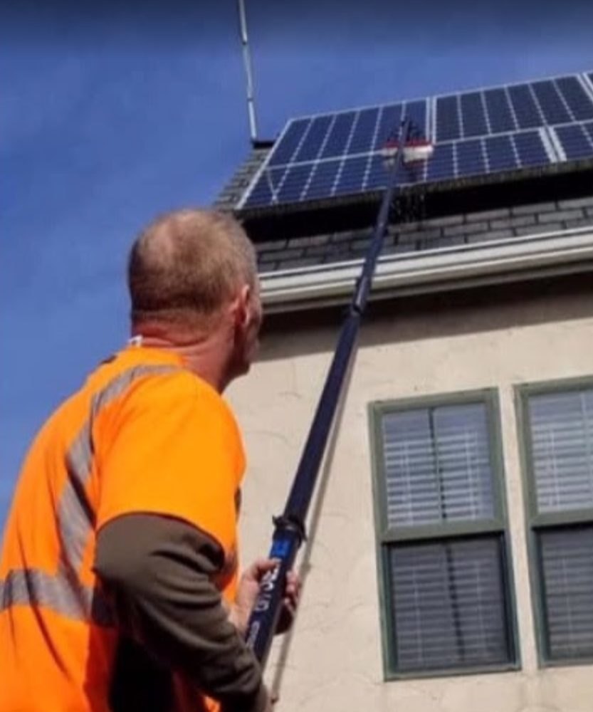 Technician cleaning rooftop solar panels with a water-fed pole