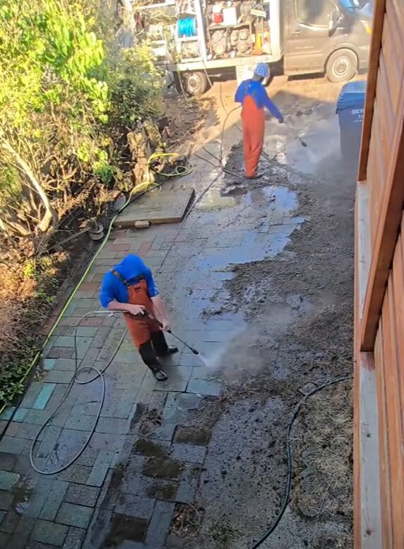 Two Deep Water technicians pressure washing a brick paver patio in Seattle